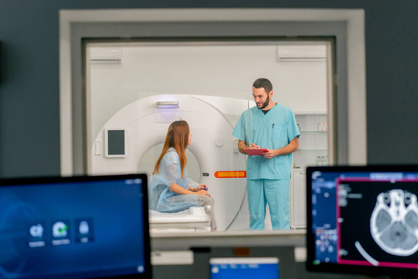 Számítógépes tomográfiás vizsgálat előtt a beteggel kommunikáló orvos hátterében diagnosztikai monitorok - Fotó, kép