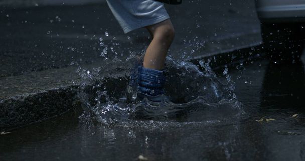Niño saltando al charco en la calle con botas de lluvia en cámara súper lenta a 800 fps capturados en alta velocidad, salpicando agua por todas partes - Foto, imagen