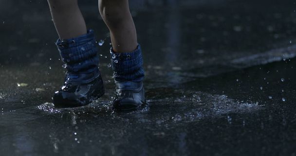 Παιδί που πατάει σε λίμνη με νερό σε πολύ αργή κίνηση φορώντας μπότες βροχής πιτσιλίζοντας σταγονίδια υγρού παντού συλλαμβάνονται με κάμερα υψηλής ταχύτητας σε 800 fps - Φωτογραφία, εικόνα