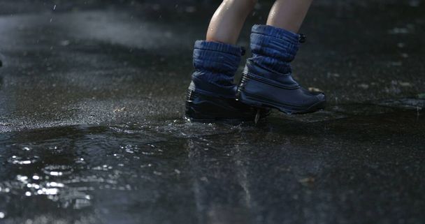Детские ступни, идущие под дождем на улице, тротуар с водяными капельками, падающими в супер замедленной съемке, захваченной высокоскоростной камерой, дождливый день - Фото, изображение