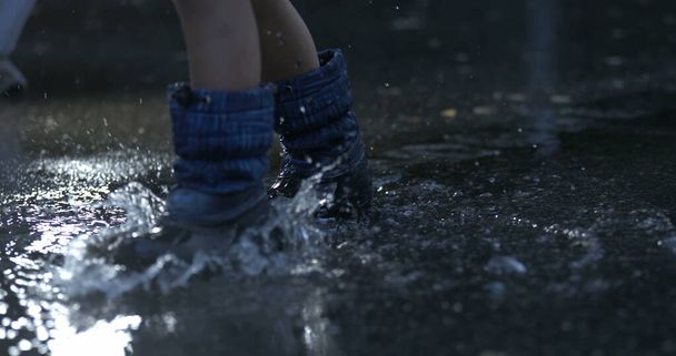 Ребенок шагает в водяной луже в супер замедленной съемке в дождевых сапогах, брызгающих капельками жидкости повсюду, заснятых высокоскоростной камерой на 800 кадров в секунду - Фото, изображение