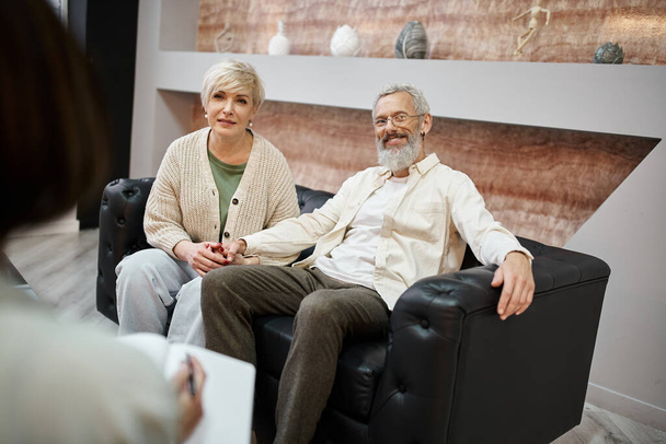 счастливая пара среднего возраста, сидящая на диване рядом с семейным психологом, поддержка отношений - Фото, изображение