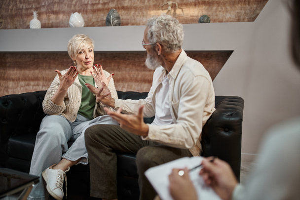 емоційна пара середнього віку сперечається, сидячи біля психолога під час сеансу терапії - Фото, зображення