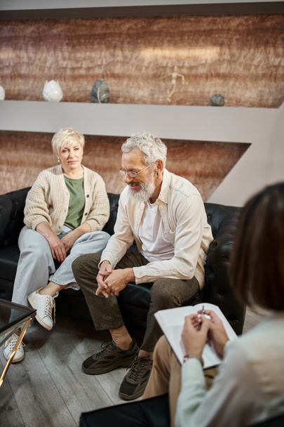 małżeństwo w średnim wieku siedzi na kanapie i omawia problem w pobliżu psychologa podczas sesji - Zdjęcie, obraz
