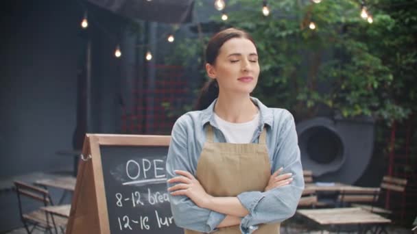 Happy Caucasian woman with pony tale standing next cafe board and cheerfully smiling. Young waitress having good feelings before working day on street bar. Outdoors. Work concept. - Footage, Video