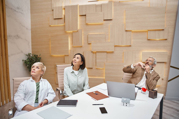Bebaarde makelaar van middelbare leeftijd in glazen met presentatie aan lgbt klanten in onroerend goed kantoor - Foto, afbeelding