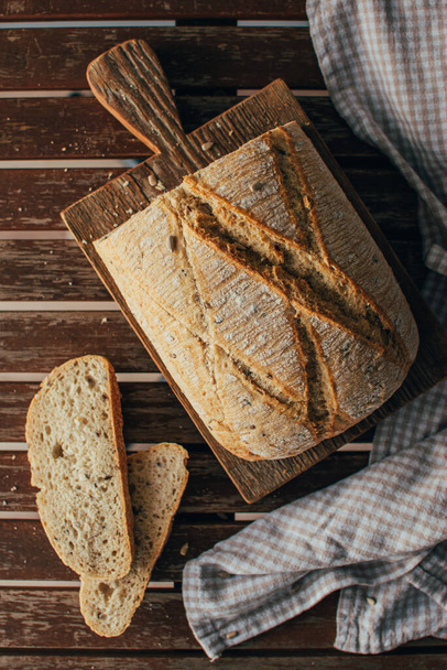 Draufsicht auf frisch gebackene Brotlaibe auf rustikalem Holzschneidebrett und Serviette - Foto, Bild