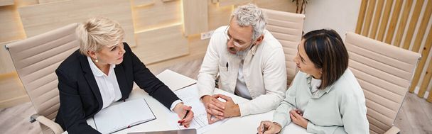 agente imobiliário feminino de meia idade discutindo projeto de nova casa com casal no escritório, banner - Foto, Imagem