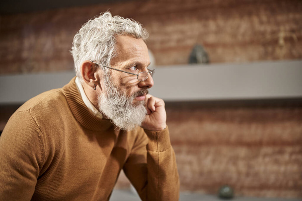 γενειοφόρος μεσήλικας ψυχολόγος με γυαλιά κοιτάζει αλλού και ακούει προσεκτικά κατά τη διάρκεια της συνεδρίας - Φωτογραφία, εικόνα