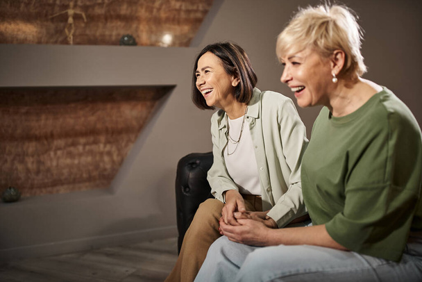 allegra coppia lesbica di mezza età sorridente mentre si siede sul divano durante la sessione di terapia - Foto, immagini