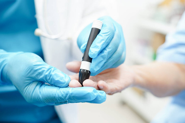 Ασιάτης γιατρός που χρησιμοποιεί συσκευή τύπου πένας lancet στο δάχτυλο του ανώτερου ασθενούς για να ελέγξει το επίπεδο σακχάρου στο αίμα για τη θεραπεία του διαβήτη. - Φωτογραφία, εικόνα