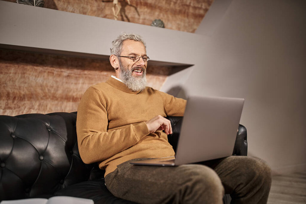 fröhlicher Psychologe mittleren Alters mit Bart spricht während Online-Beratung mit Klient am Laptop - Foto, Bild