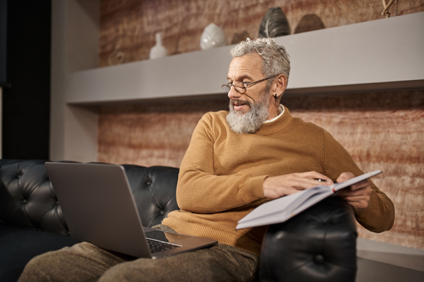 Бородатый психолог средних лет в очках разговаривает с клиентом во время онлайн-консультации на ноутбуке - Фото, изображение