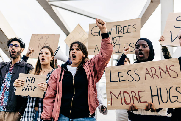 Zróżnicowana grupa aktywistów trzymająca plakaty i transparenty antywojenne protestujące przeciwko wojnie i przemocy na świecie. - Zdjęcie, obraz