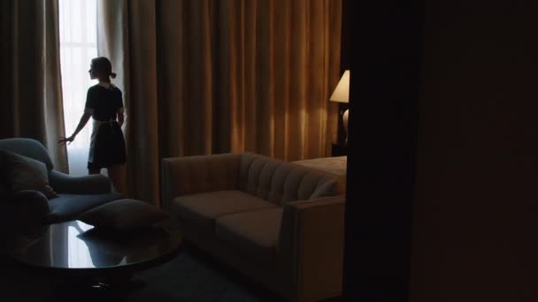 Długie ujęcie pokojówki przygotowującej pokój do odprawy, zakładającej tabletki na sofę i otwierającej zasłony w hotelu - Materiał filmowy, wideo