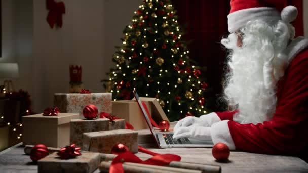 Święty Mikołaj pisze na komputerze pod choinką. - Materiał filmowy, wideo