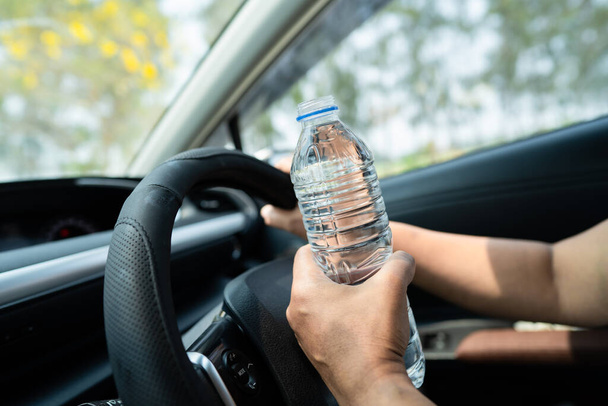 Azjatka kierowca trzyma butelkę wody pitnej podczas jazdy samochodem. Plastikowa butelka gorącej wody powoduje pożar. - Zdjęcie, obraz