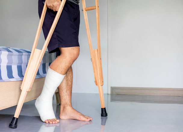 Zbliżenie pacjenta ze złamaną nogą w gipsie i bandażu, mężczyzna ze drzazgą na nodze spaceruje z kulami w domu - Zdjęcie, obraz