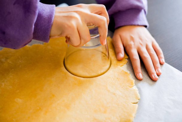 Captura la alegría como las manos de un niño hábilmente cortar masa cruda con un vaso, embarcarse en un delicioso viaje de hornear para crear encantadoras mini tartas - Foto, imagen