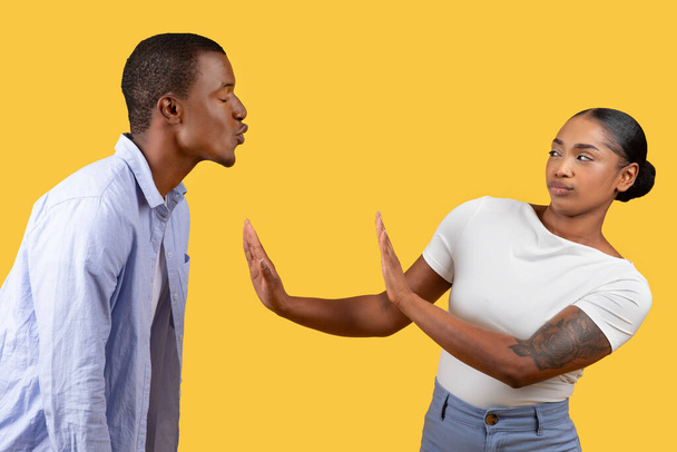 Homme noir tente baiser tandis que la femme lève la main dans le panneau stop, mettant en valeur le désaccord ou le cadre de frontière, fond jaune - Photo, image