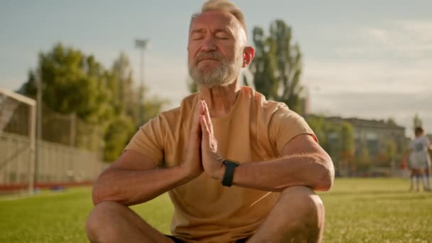 Stary Europejczyk zamknięte oczy medytacji na trawie w mieście relaks zdrowe ciało umysł starsi sportowcy zewnątrz modlić joga zen równowaga pokój praktyka energetyczna stanowią lotos na zewnątrz dobre samopoczucie sport - Materiał filmowy, wideo