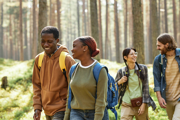 外の森で話したり一緒に歩いたりする若者の多民族グループ - 写真・画像