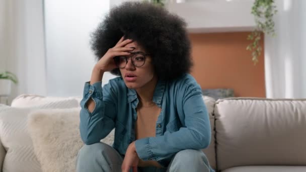 Smutný frustrovaný znepokojen úzkostlivý stresovaný etnický dívka biracial depressed žena zmatený afroameričanka žena na gauči doma myšlení problém řešení rozhodnutí tření držení hlavy bolest hlavy - Záběry, video