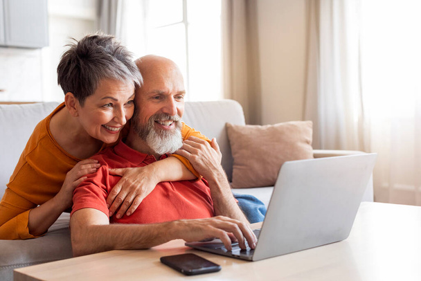 Glückliches Senior-Paar mit Laptop-Computer, Surfen im Internet zu Hause, ältere Ehepartner Online-Einkauf zusammen, Einkauf im Internet und Entspannung im Wohnzimmer Innenraum, Kopierraum - Foto, Bild