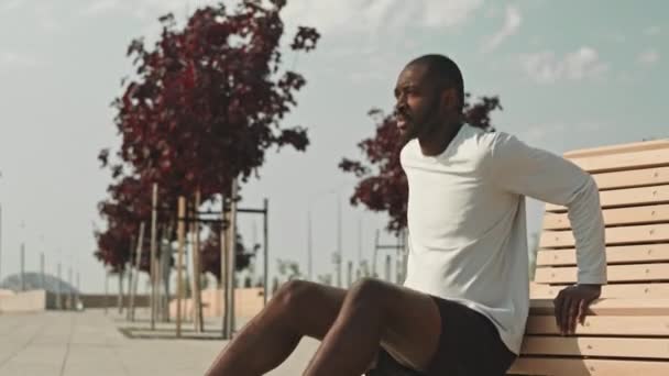 Tilt up shot młodego czarnego człowieka robi triceps dips ćwiczenia przy ławce ulicznej na świeżym powietrzu w mieście podczas porannego treningu - Materiał filmowy, wideo