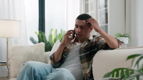 Smutne zdenerwowany zszokowany sfrustrowany zaniepokojony Afroamerykanin etniczny birasowy zestresowany mężczyzna rozmawiający telefon w domu problem słyszenie złe wiadomości szok kłopoty smartfon rozmowa negatywne rozmowy - Materiał filmowy, wideo