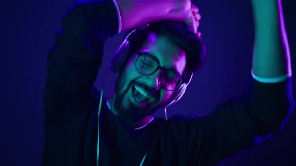 Aufgeregte indische Kerl tanzen lustigen Tanz bewegt sich mit den Händen zur Musik in Neon-Nachtclub muslimischen Mann lachen genießen Musiktitel Audio glücklich freudig Spaß haben arabische Mann hören Lied in Kopfhörer - Filmmaterial, Video
