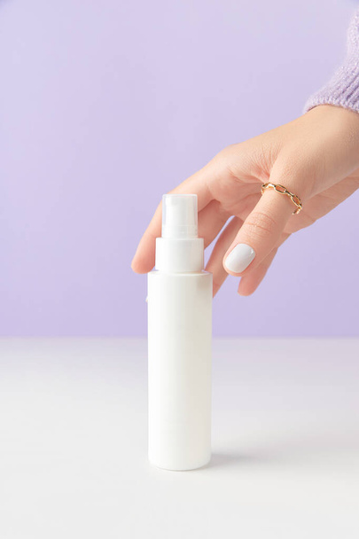 Womans mano toccare tubo bottiglia bianca su sfondo lilla. Self care concetto di trattamento di bellezza. Prodotti per la cura accessori bagno. - Foto, immagini