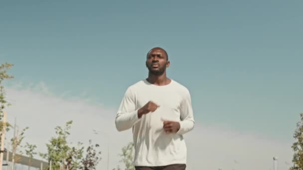 Basso angolo rallentatore colpo di atletico nero uomo che fa jogging all'aperto durante l'allenamento al mattino con cielo nuvoloso - Filmati, video