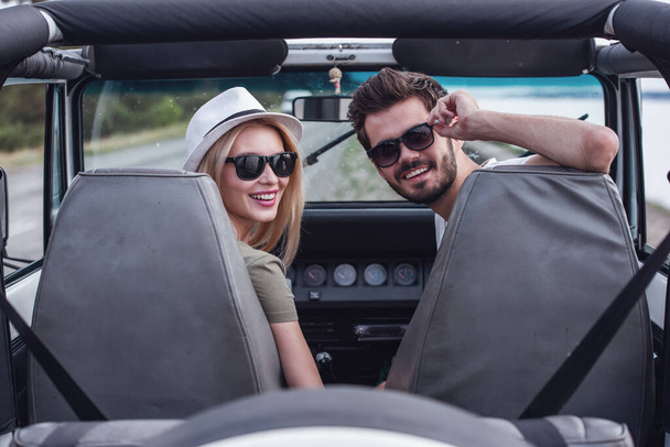 Kaunis nuori pari katselee kameraa ja hymyilee matkustaessaan autolla
 - Valokuva, kuva