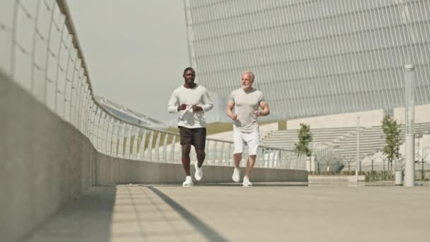 Zeitlupenaufnahme von älteren und jungen Männern, die gemeinsam in Richtung Kamera joggen, während sie tagsüber in der Stadt trainieren - Filmmaterial, Video
