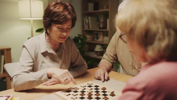 Over de schouder schot, ouderen proberen om elkaar te winnen in dammen zitten aan tafel samen thuis - Video