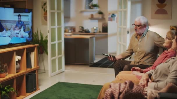 Medium long shot di gruppo di pensionati che discutono di film mentre lo guardano insieme in TV mentre sono seduti sul divano in soggiorno - Filmati, video