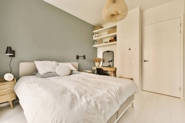 un dormitorio con una cama, vestidor y lámpara en la pared detrás de ella es una puerta blanca abierta que conduce a otra habitación - Foto, Imagen