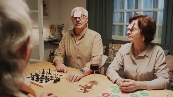 Over the shoulder shot, pensioners playing funny game guessing who they are with stickers on foreheads at home party - Footage, Video