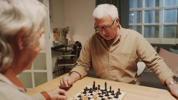 Over de schouder van geconcentreerde positieve oudere mannen die thuis schaken - Video