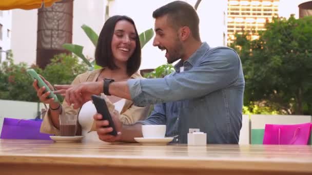 Prodej, nakupování, konzumace, volný čas a lidé koncept - šťastný pár při pohledu na aplikaci na mobilní telefon nákupní tašky pití kávy v nákupním centru - Záběry, video
