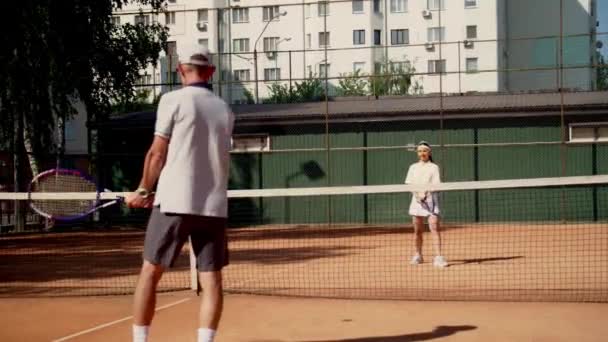 Mies valmentaja osaston tyttö suorittaa yhteisen koulutuksen tennis asetettu keskimäärin intensiteetti. Palveleva ja taipuisa iskuja mailat. Nuori nainen urheilija johdolla kouluttaja valmistautuu - Materiaali, video