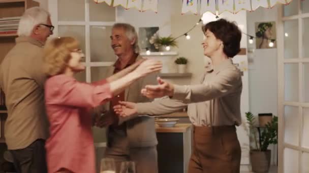 Средний снимок веселых пожилых друзей, обнимающих друг друга при встрече на праздновании дня рождения в уютной квартире на вечеринке - Кадры, видео