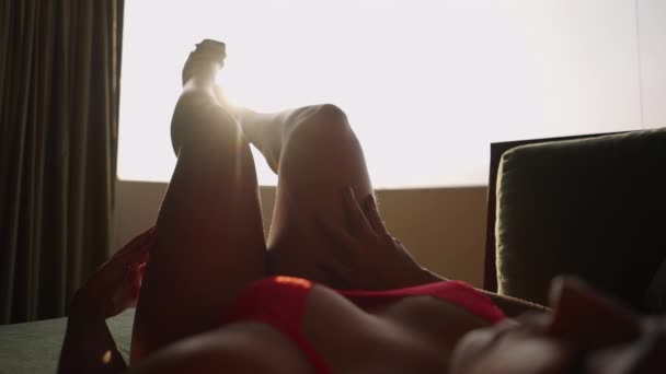Altın tenli kadın arka plandaki pencere ışığıyla bacaklarına dokunuyor. - Video, Çekim