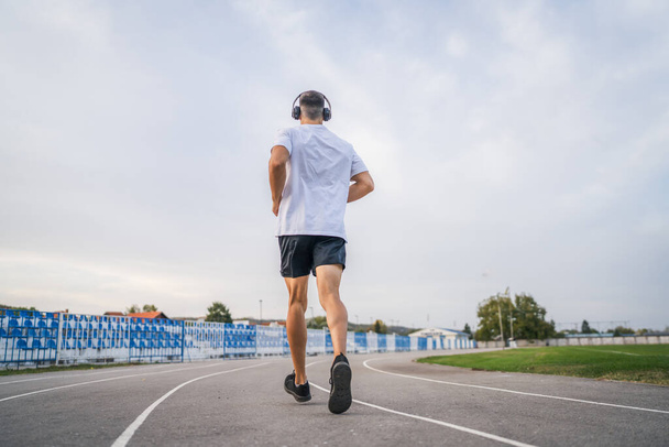 dorosłych kaukaski mężczyzna jogging na bieżni męski sportowiec na stadionie szkolenia uruchomić w słoneczny wiosna lub lato dzień prawdziwe ludzie zdrowy styl życia koncepcja - Zdjęcie, obraz