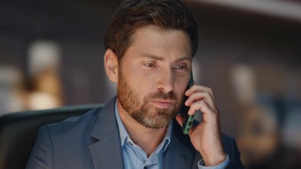 Closeup smiling man talking phone with smile at dark place. Handsome cheerful brunette ceo speaking modern smartphone sitting evening room. Bearded happy director using telephone enjoying work call - Footage, Video