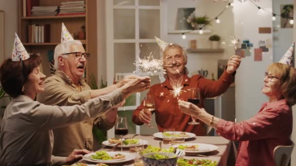 Medium long shot di amici anziani positivi che festeggiano il compleanno con luci bengala a casa festa - Filmati, video