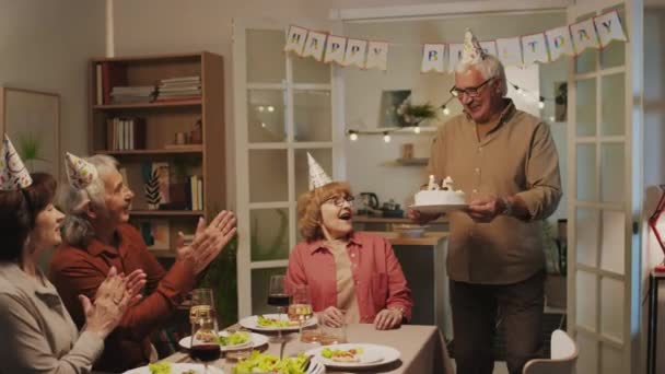 Довгий знімок позитивного старшого чоловіка, що приносить торт на день народження дружині, і вона вибухає свічки у формі шістдесяти п'яти на домашній вечірці - Кадри, відео