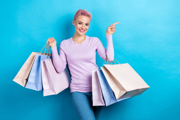 Portrait of positive woman wear stylish sweatshirt hold new clothes indicating at sale empty space isolated on blue color background. - Фото, изображение