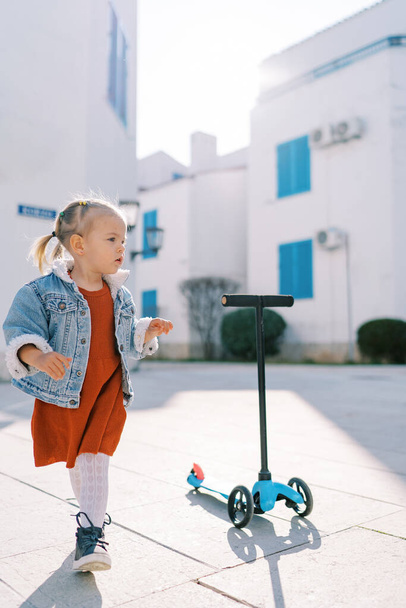 Ein kleines Mädchen läuft auf der Straße im Hof des Hauses neben dem stehenden Motorroller. Hochwertiges Foto - Foto, Bild